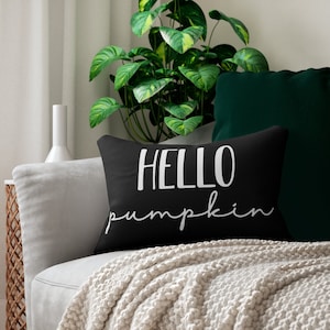 May include: Black throw pillow with white text that reads "HELLO pumpkin". The pillow is on a gray couch with a white blanket.