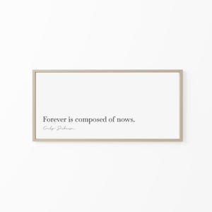 May include: A framed print with the quote "Forever is composed of nows." by Emily Dickinson. The text is in a simple, elegant font, centered on a white background. The frame is a light, neutral color.