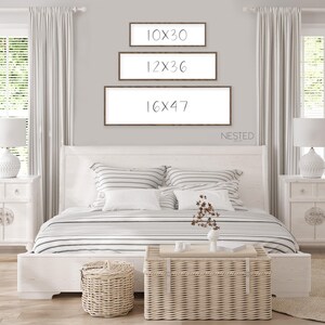 May include: Three framed prints with the text "10x30", "12x36", and "16x47" hanging on a white wall above a white bed with a striped comforter. The text "NESTED" is below the prints.