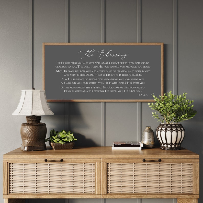 Peut inclure: Une &oelig;uvre d'art encadr&eacute;e avec le texte "The Blessing" en &eacute;criture &eacute;l&eacute;gante. L'&oelig;uvre est expos&eacute;e au-dessus d'une console en bois avec une lampe, de la verdure et des objets d&eacute;coratifs. Le mur est peint en gris neutre.