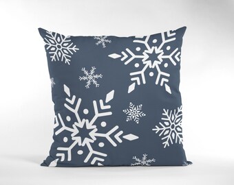 May include: A square decorative pillow with a dark blue background and a repeating pattern of white snowflakes. The snowflakes vary in size and design, creating a winter holiday theme. The pillow is likely made of a soft fabric.