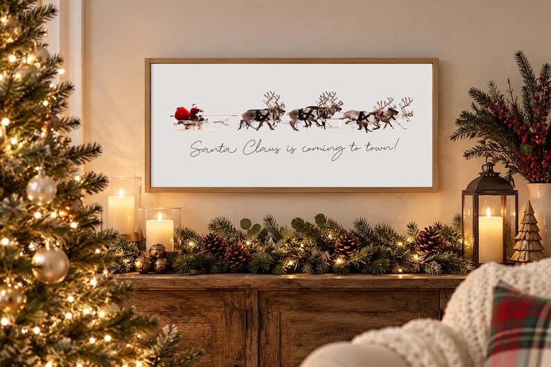 Puede incluir: Un cuadro rectangular con marco de madera clara que presenta un fondo blanco con un gr&aacute;fico de Santa Claus en un trineo tirado por cuatro renos. El texto Santa Claus is coming to town est&aacute; impreso en letra cursiva de color negro.