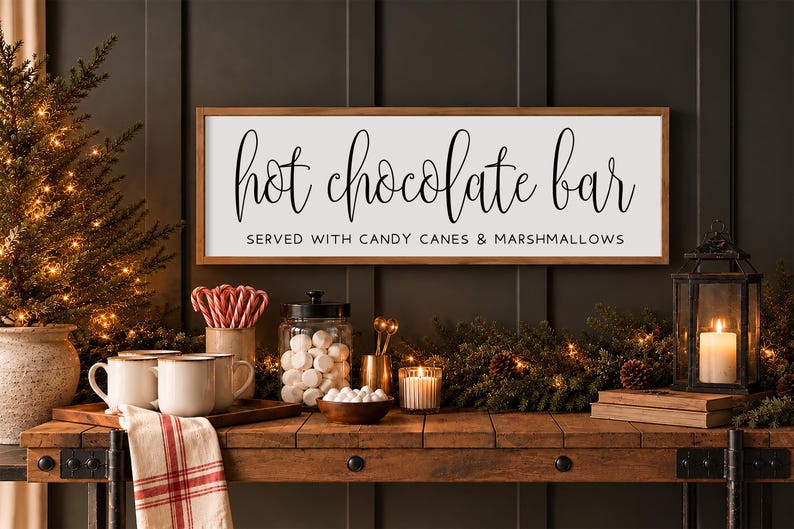 May include: A rectangular wooden sign with a white background and a brown frame featuring the black text "hot chocolate bar" in a script font and "SERVED WITH CANDY CANES & MARSHMALLOWS" in a simple sans-serif font.