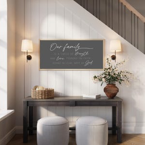 May include: A rectangular wall sign with a dark gray background and a light wood frame. The sign features white text that reads: Our family is a circle of strength and love, founded on faith, joined in love, kept by God.