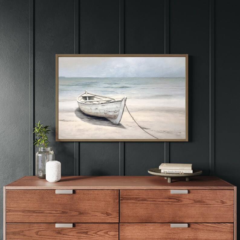 Framed wall art with wood frame featuring a neutral-toned rowboat on a beach with ocean waves in the background, perfect for coastal home decor.