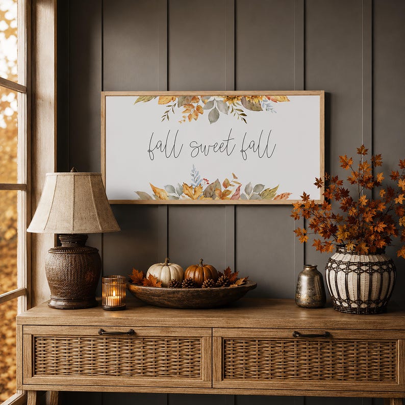 A rectangular wooden framed sign with the words "fall sweet fall" in cursive script. The sign is decorated with watercolor leaves in shades of brown, beige, and green.