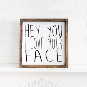 K&ouml;nnte beinhalten: Ein Holzschild mit dem Text "Hey You I Love Your Face" in schwarzen Buchstaben.