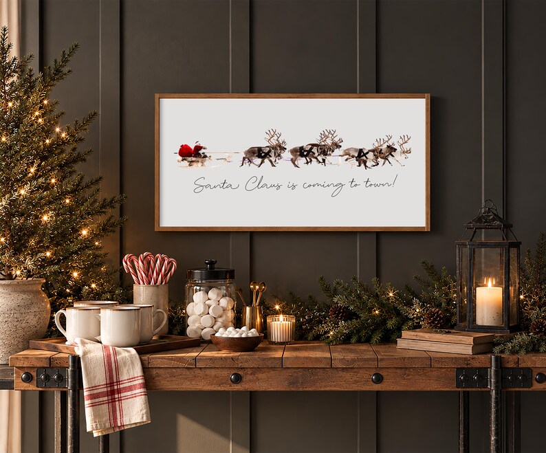 Puede incluir: Un letrero de pared rectangular con marco de madera que presenta un gr&aacute;fico de Santa Claus en un trineo tirado por renos y el texto Santa Claus is coming to town! El letrero se muestra en una pared oscura sobre una mesa de madera con decoraci&oacute;n.