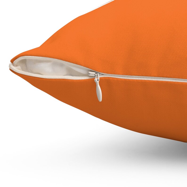 K&ouml;nnte beinhalten: Nahaufnahme eines orangen Kissens mit einem wei&szlig;en Rei&szlig;verschluss. Der Rei&szlig;verschluss ist ge&ouml;ffnet und das Kissen liegt flach.