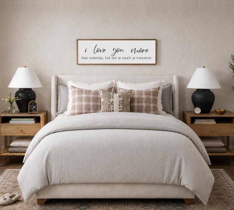Puede incluir: Una escena de dormitorio con una cama con un edred&oacute;n gris claro y almohadas decorativas. Dos mesitas de noche de madera flanquean la cama, cada una con una l&aacute;mpara y decoraci&oacute;n. Un letrero enmarcado sobre la cama dice "i love you more than yesterday, but not as much as tomorrow."