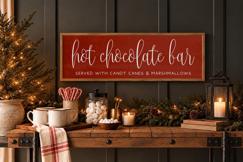 May include: A rectangular wooden sign with a red background and a light wood frame. The text reads "hot chocolate bar" in white script and "SERVED WITH CANDY CANES & MARSHMALLOWS" in white block letters. The sign is mounted on a dark wall.