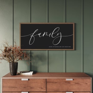 May include: A rectangular wall sign with a dark brown wooden frame and a black background. The word family is written in large white cursive script, with the text WHERE LIFE BEGINS AND LOVE NEVER ENDS printed in smaller white capital letters.