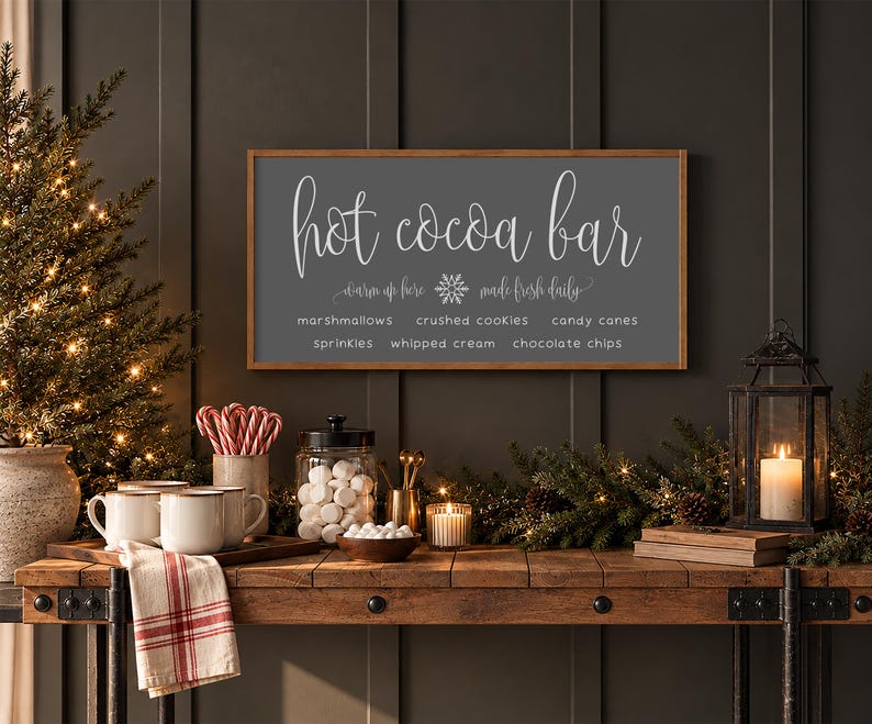 May include: A rectangular wall sign with a dark gray background and a light wood frame. The text reads: hot cocoa bar, warm up here, made fresh daily, marshmallows, crushed cookies, candy canes, sprinkles, whipped cream, chocolate chips.
