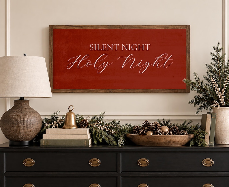 May include: A rectangular wall sign with a dark wood frame and a deep red background. The text "SILENT NIGHT" is printed in a white sans-serif font, and the words "Holy Night" are written below in a white, elegant, flowing script font.