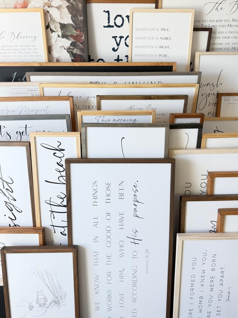 Puede incluir: Una colecci&oacute;n de letreros de pared rectangulares con marcos de madera, fondos blancos y texto e ilustraciones impresos en negro. Los letreros muestran varias citas inspiradoras, vers&iacute;culos y frases en diversas fuentes, dispuestos en una pila superpuesta.