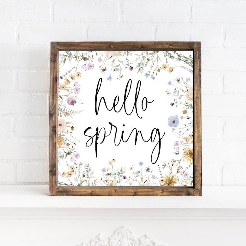 May include: A framed print with a white background and a floral border. The text "hello spring" is written in black cursive script in the center of the print.