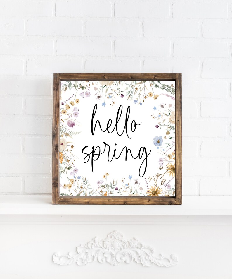 May include: A framed print with a white background and a floral border. The text "hello spring" is written in black cursive lettering.