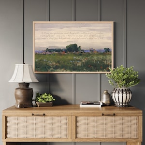 May include: A framed landscape print with a light wood frame hangs above a wooden console table. The print depicts a field with trees and a quote from Ephesians 2:8-10. A lamp, plants, and decorative items are on the table.