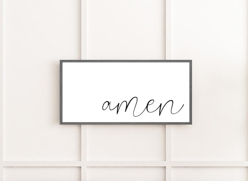 May include: A rectangular wall sign featuring a dark gray frame and a white background. The word amen is written in the center in a black, lowercase, cursive script font. The sign is oriented horizontally and has a clean, simple design.