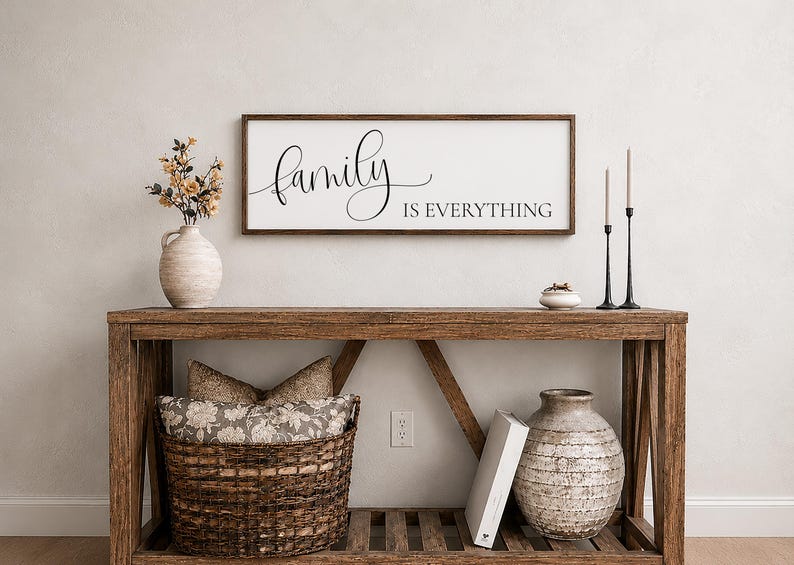 May include: A rectangular wooden framed wall sign with a white background and black text that reads "family IS EVERYTHING". The word family is in a cursive script font, while IS EVERYTHING is in a clean, capitalized sans-serif typeface.