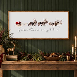 Puede incluir: Un letrero de pared rectangular con marco de madera que muestra un gr&aacute;fico de Santa Claus en un trineo tirado por renos sobre un fondo blanco. El texto "Santa Claus is coming to town!" est&aacute; impreso en cursiva negra debajo.