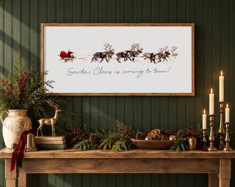 May include: A rectangular wall sign with a wooden frame featuring a white background, a graphic of Santa Claus in a sleigh pulled by reindeer, and the black cursive text "Santa Claus is coming to town!" centered below the illustration.