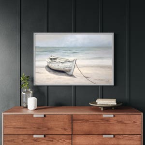 Framed wall art with wood frame featuring a neutral-toned rowboat on a beach with ocean waves in the background, perfect for coastal home decor.