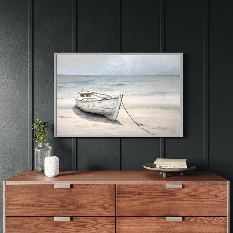 Framed wall art with wood frame featuring a neutral-toned rowboat on a beach with ocean waves in the background, perfect for coastal home decor.