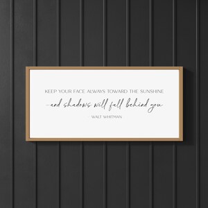 K&ouml;nnte beinhalten: Gerahmter Druck mit einem hellbraunen Holzrahmen. Der Druck zeigt das Zitat "KEEP YOUR FACE ALWAYS TOWARD THE SUNSHINE -and shadows will fall behind you" von Walt Whitman, in schwarzer, eleganter Schrift auf wei&szlig;em Hintergrund.