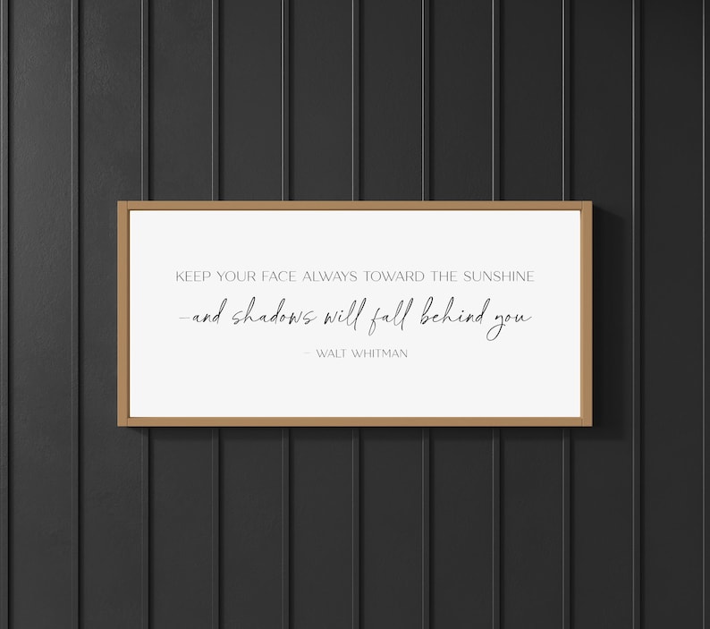 K&ouml;nnte beinhalten: Gerahmter Druck mit einem hellbraunen Holzrahmen. Der Druck zeigt das Zitat "KEEP YOUR FACE ALWAYS TOWARD THE SUNSHINE -and shadows will fall behind you" von Walt Whitman, in schwarzer, eleganter Schrift auf wei&szlig;em Hintergrund.