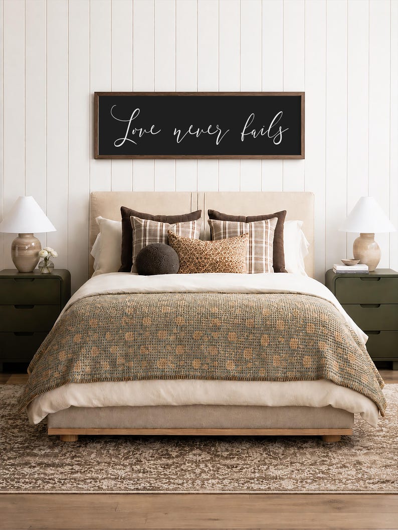 May include: A bedroom scene featuring a bed with a beige headboard, layered bedding, and decorative pillows. A dark wooden framed sign above the bed reads "Love never fails" in white script. Two green nightstands with lamps flank the bed.