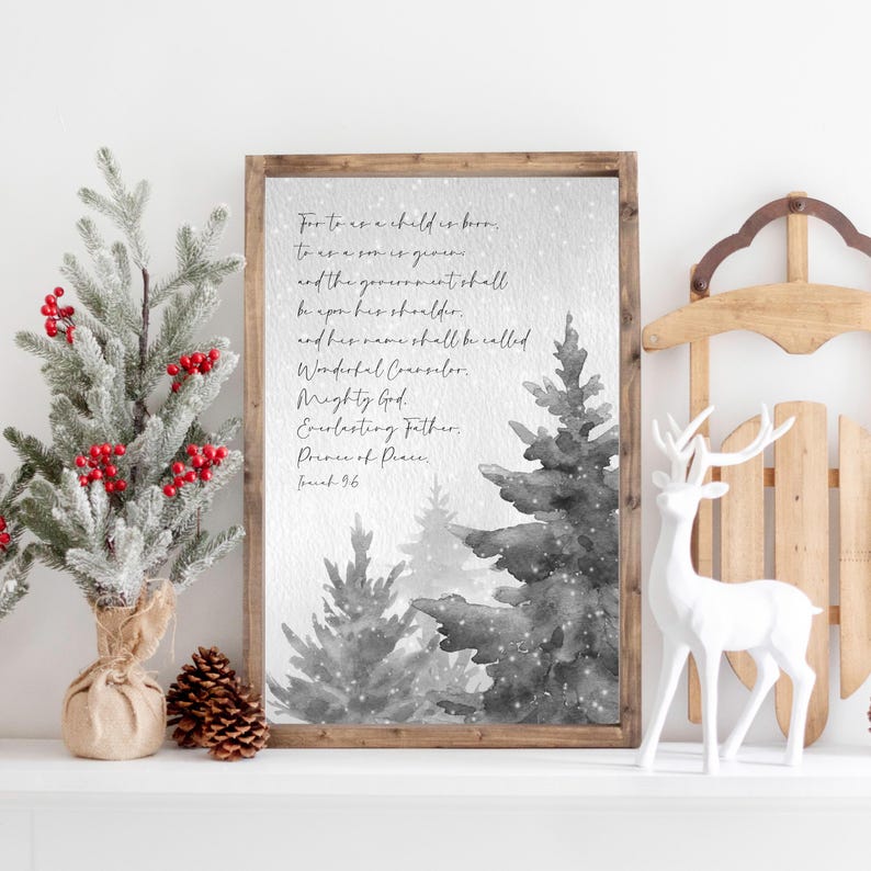 May include: A framed print with a winter scene and text from Isaiah 9:6. The artwork features grayscale watercolor trees and a wooden frame. Decorative elements include a small Christmas tree with red berries, pine cones, a white deer figurine, and a wooden sled.