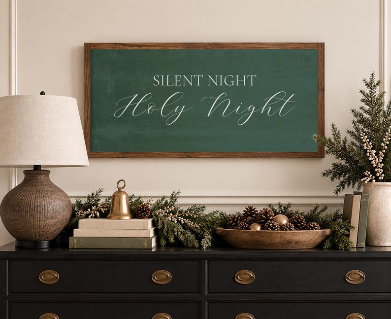 May include: A rectangular wall sign with a dark green background and a brown wooden frame. The text SILENT NIGHT is printed in a simple sans-serif font, while the words Holy Night are written below in a white, elegant, flowing script font.