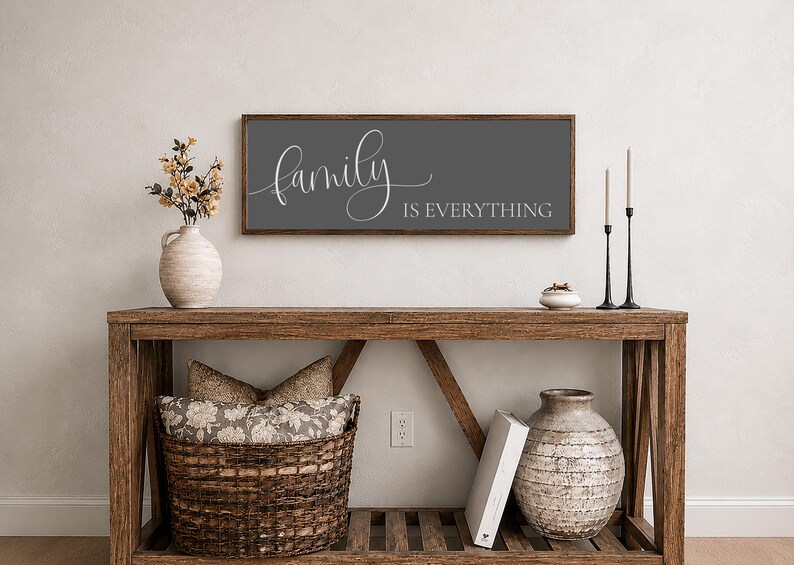 May include: A rectangular wall sign with a dark gray background and a wooden frame. The text "family IS EVERYTHING" is printed in white, with the word "family" in a cursive script font and "IS EVERYTHING" in a clean, uppercase sans-serif font.