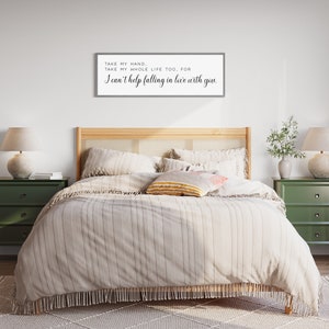 Op de afbeelding: Een slaapkamer met een bed met een licht gestreept dekbed en decoratieve kussens. Twee groene nachtkastjes met lampen staan aan weerszijden van het bed. Een ingelijst bord boven het bed luidt: "TAKE MY HAND. TAKE MY WHOLE LIFE TOO, FOR I can't help falling in love with you."