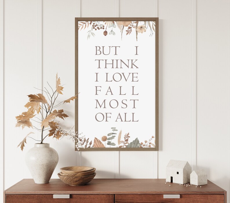 Puede incluir: Una l&aacute;mina de arte mural rectangular en un marco marr&oacute;n con el texto BUT I THINK I LOVE FALL MOST OF ALL en letras may&uacute;sculas marrones. El dise&ntilde;o incluye ilustraciones bot&aacute;nicas de hojas secas, bayas y tallos en la parte superior e inferior.