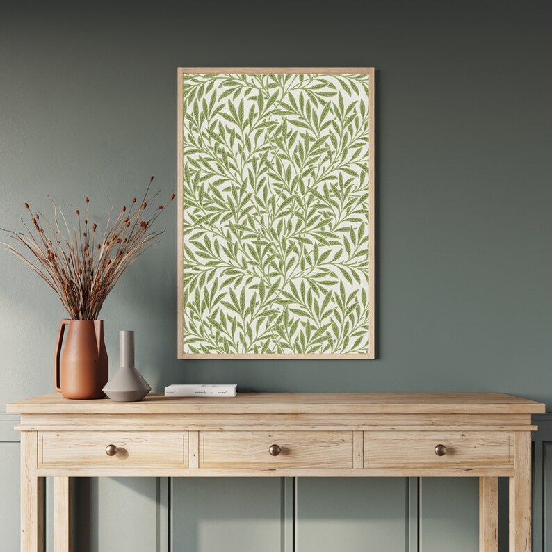 A framed print of a green and white floral pattern with a repeating design of leaves and branches. William Morris botanical wall art with green leaf pattern