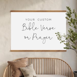 May include: A rectangular white wall hanging featuring the black text YOUR CUSTOM Bible Verse or Prayer. The print is secured between two horizontal wooden bars at the top and bottom, creating a clean display for personalised wall art.
