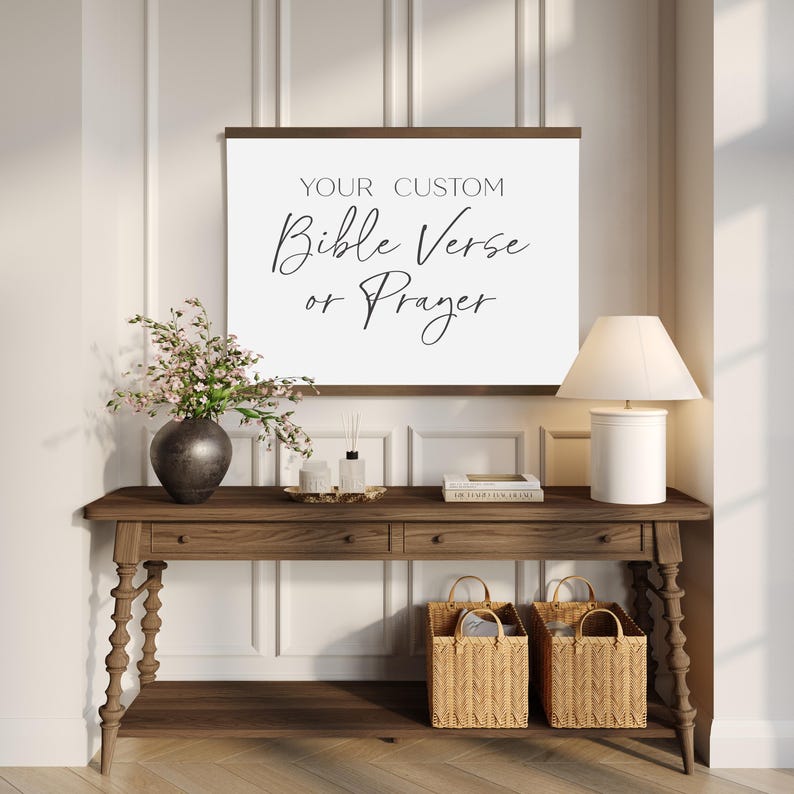 May include: A rectangular wall hanging featuring a dark wood frame and a white canvas background. The text printed in black reads: YOUR CUSTOM Bible Verse or Prayer. The piece is displayed above a wooden console table with two woven baskets.