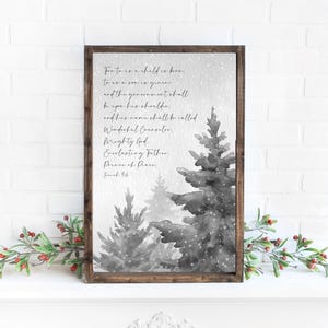 May include: A framed print featuring a watercolor illustration of grayscale Christmas trees with falling snow. The print includes the text of Isaiah 9:6, a religious passage, in elegant script. The frame is a dark brown color.