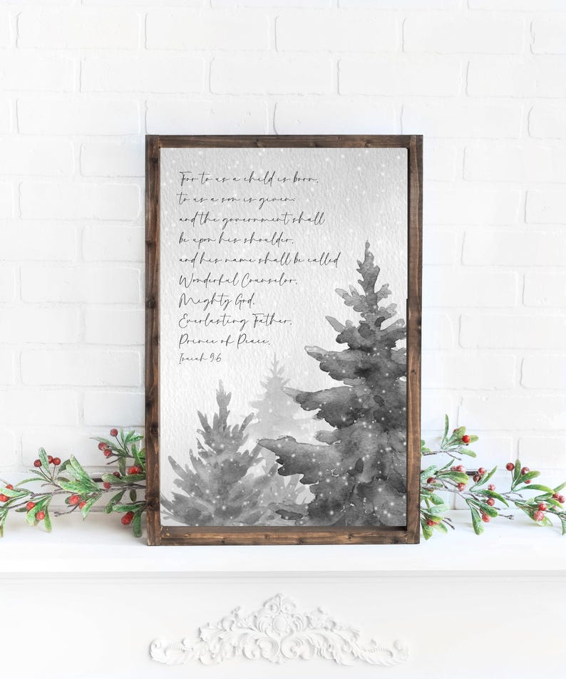 May include: A framed print featuring a watercolor illustration of grayscale Christmas trees with falling snow. The print includes the text of Isaiah 9:6, a religious passage, in elegant script. The frame is a dark brown color.