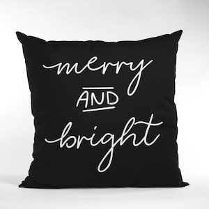 Puede incluir: Coj&iacute;n negro con texto blanco que dice "merry and bright".