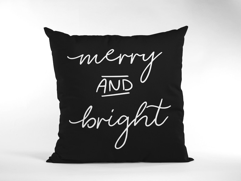 Puede incluir: Coj&iacute;n negro con texto blanco que dice "merry and bright".