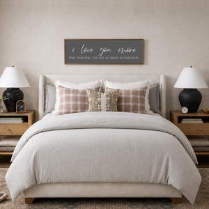 Puede incluir: Una escena de dormitorio con una cama con un edred&oacute;n gris claro y almohadas decorativas. Un letrero de madera sobre la cama dice "I love you more than yesterday, but not as much as tomorrow." Dos mesitas de noche con l&aacute;mparas completan la escena.