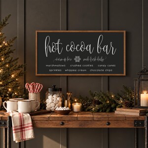 May include: A rectangular wooden sign with a dark gray background and a light brown frame. The text reads: Hot cocoa bar, warm up here, made fresh daily, marshmallows, crushed cookies, candy canes, sprinkles, whipped cream, chocolate chips.