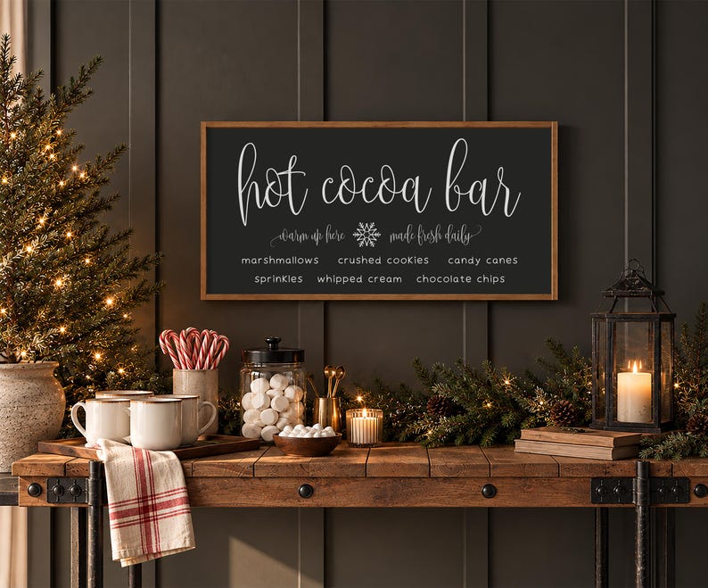 May include: A rectangular wooden sign with a dark gray background and a light brown frame. The text reads: Hot cocoa bar, warm up here, made fresh daily, marshmallows, crushed cookies, candy canes, sprinkles, whipped cream, chocolate chips.