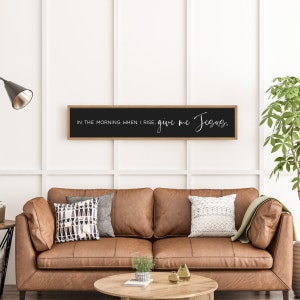 May include: A black framed sign with the text "In the morning when I rise, give me Jesus." hanging on a white wall above a brown leather couch.