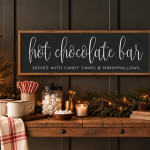 May include: A rectangular wooden sign with a dark background and a light wood frame. The text reads "hot chocolate bar" in a white script font, with "SERVED WITH CANDY CANES & MARSHMALLOWS" in a smaller, white, sans-serif font.