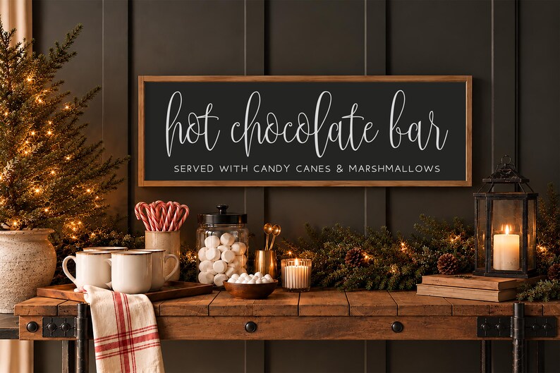 May include: A rectangular wooden sign with a dark background and a light wood frame. The text reads "hot chocolate bar" in a white script font, with "SERVED WITH CANDY CANES & MARSHMALLOWS" in a smaller, white, sans-serif font.