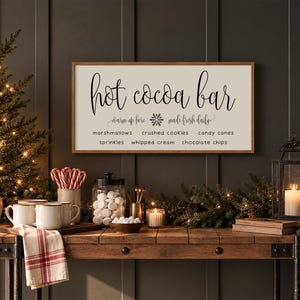 May include: A rectangular wooden sign with a white background and a brown frame featuring the black text Hot cocoa bar, warm up here, made fresh daily, and a list of toppings including marshmallows, crushed cookies, candy canes, sprinkles, whipped cream, and chocolate chips.